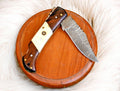 Handmade Damascus steel pocket knife with rosewood handle and bone accents, showcasing intricate blade details and craftsmanship.