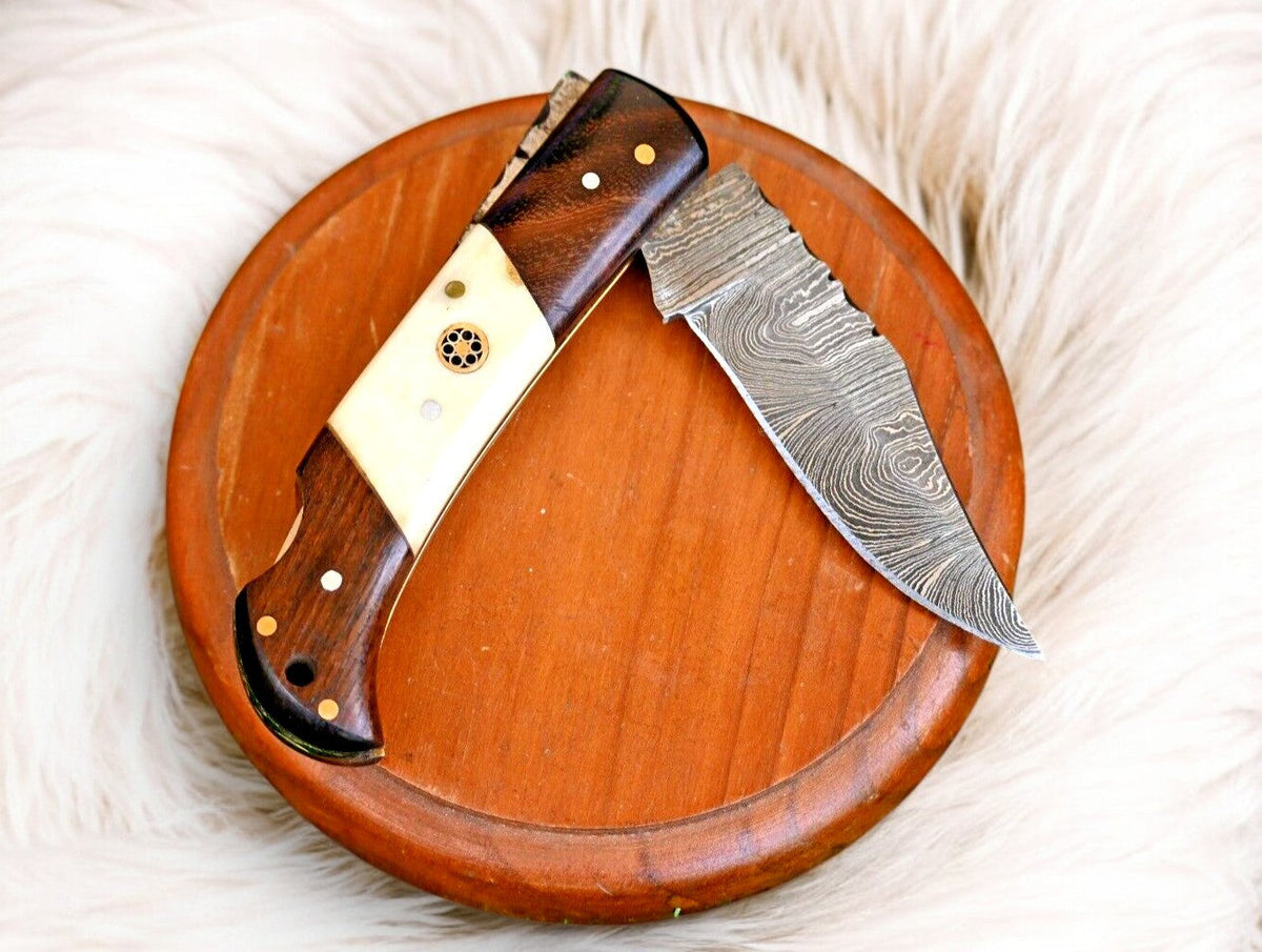 Handmade Damascus steel pocket knife with rosewood handle and bone accents, showcasing intricate blade details and craftsmanship.