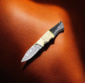 Handmade Damascus pocket knife with bone and buffalo horn handle, featuring a detailed steel blade and crafted by Damascus Knife Store