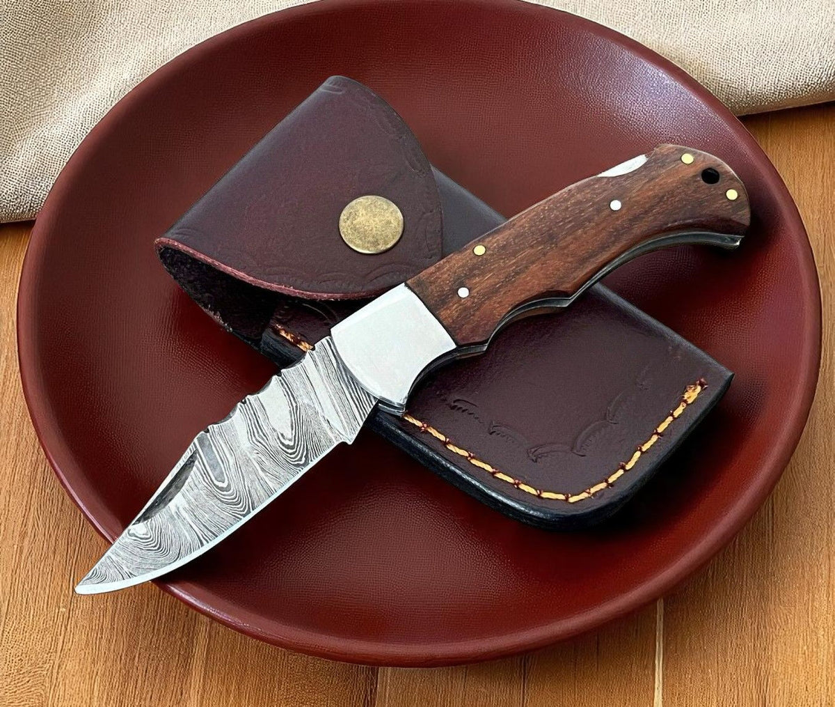 Handmade pocket knife with a wood handle and Damascus steel blade, featuring intricate patterning and craftsmanship.